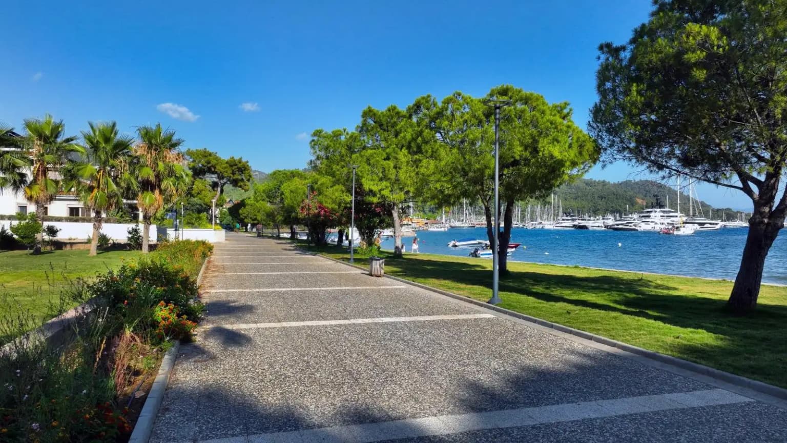 Menschen, die auf der Uferpromenade (Kordon) von Göcek spazieren gehen. Eine angenehme Spazierroute, besonders abends, begleitet von Booten im Jachthafen und Restaurants.