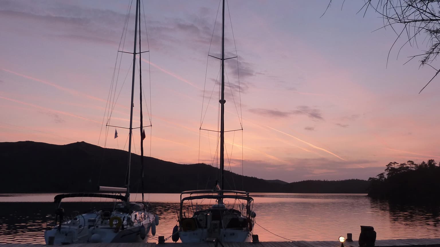 The silhouette of a boat moored to a pier at sunset in a coastal town in the Aegean. A peaceful evening view with a calm sea and warm colors.