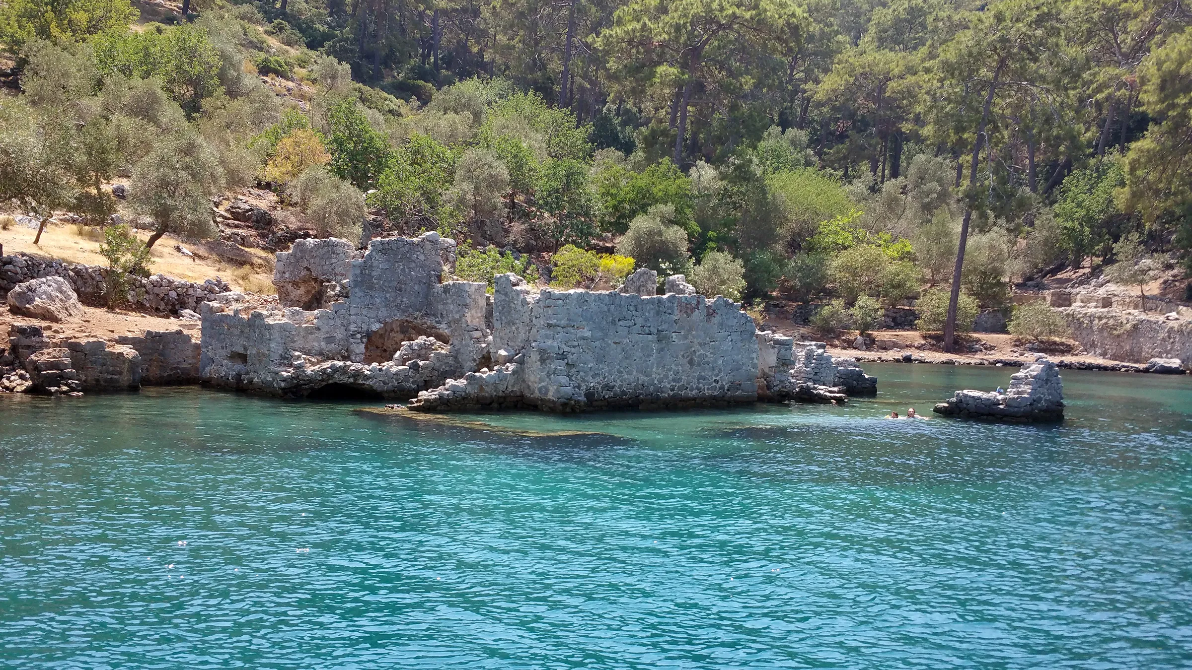 Göcek'teki Kleopatra Hamam Koyu'nun turkuaz suları ve batık manastır kalıntıları. Mavi yolculuk tekneleri için popüler yüzme ve tarih noktası.