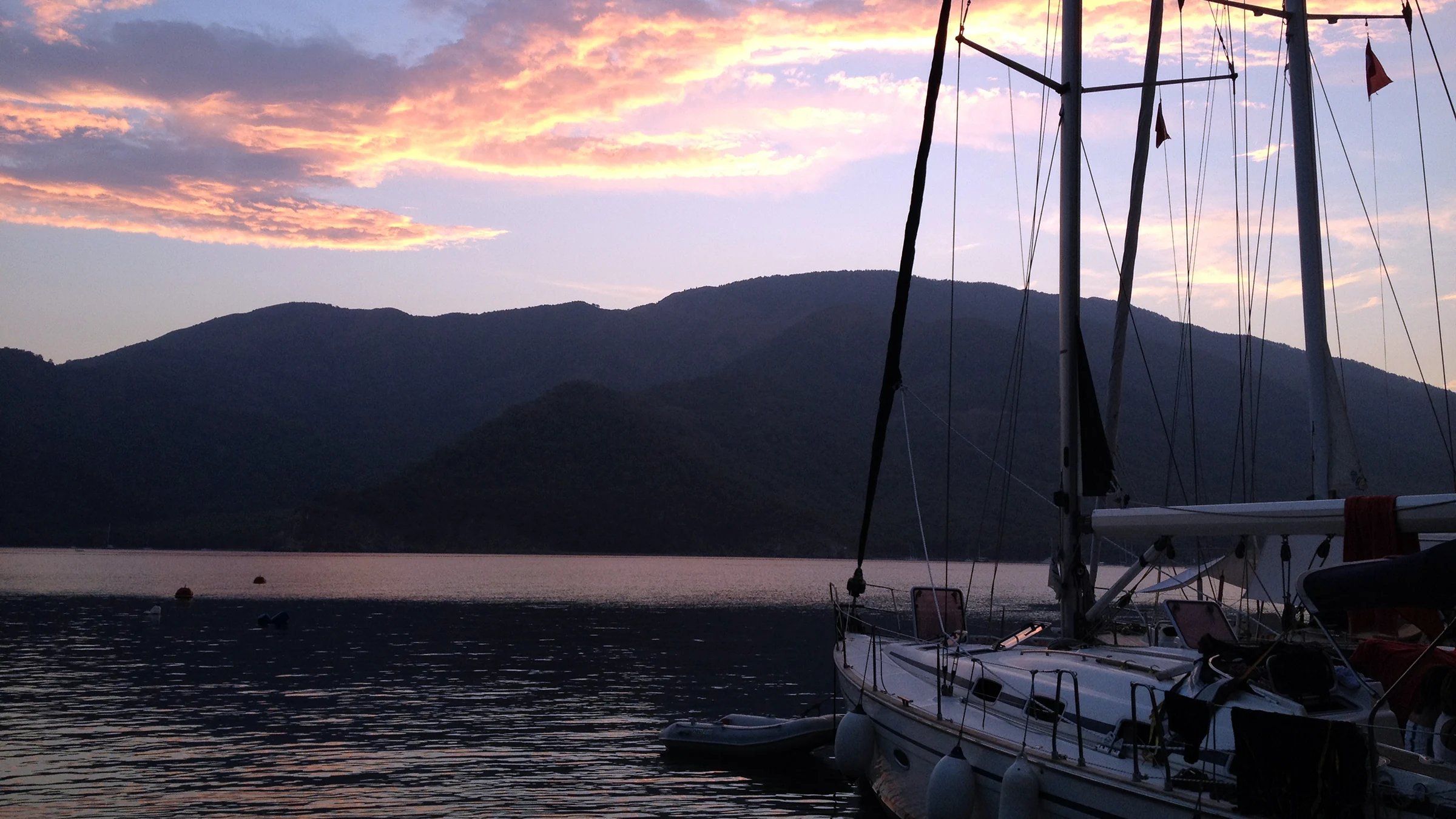 Ege koylarında gün batımında iskeleye bağlı bir yelkenli tekne. Huzurlu ve romantik bir sahil manzarası.