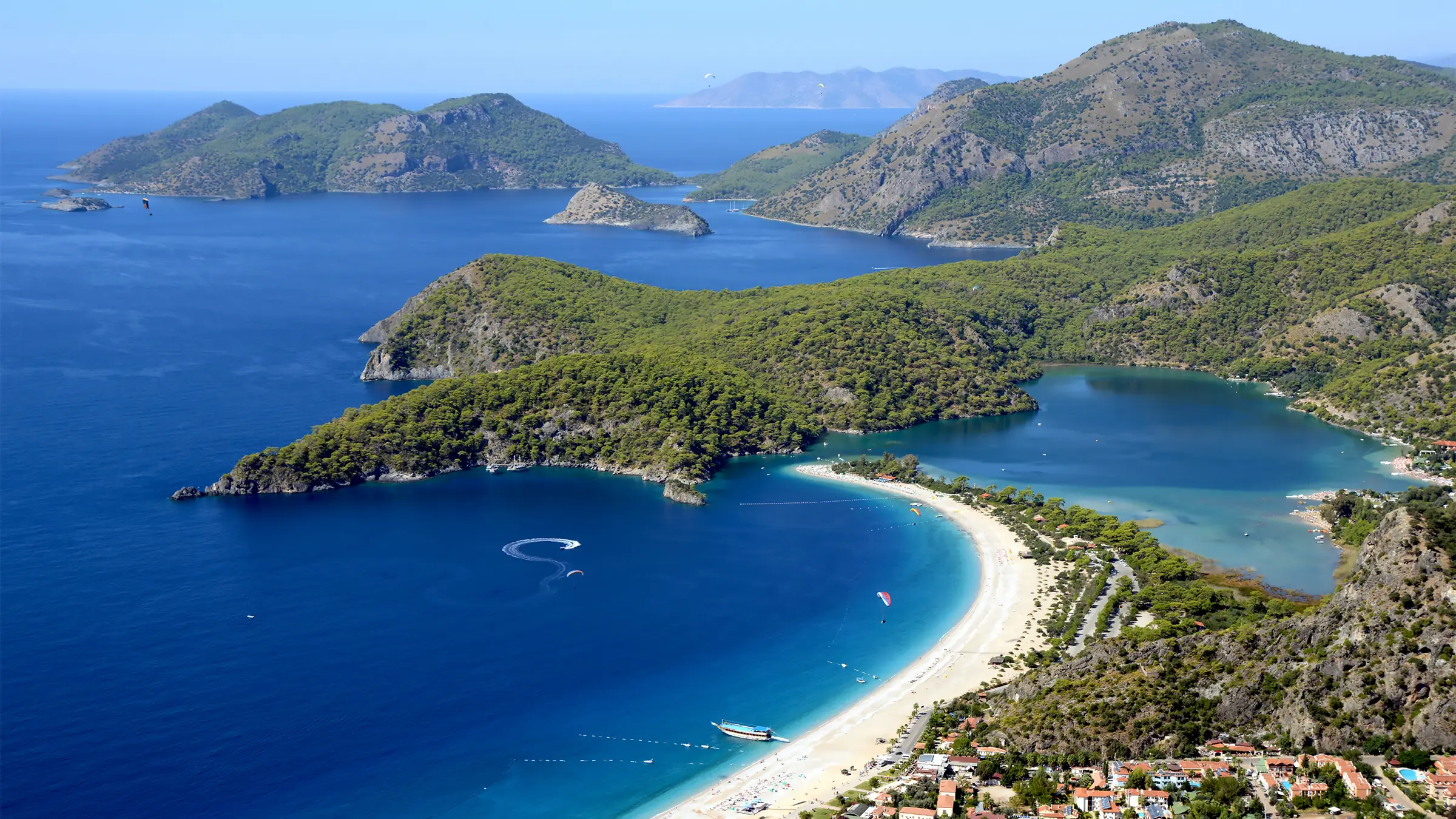 Fethiye'deki Ölüdeniz'in havadan görünümü; meşhur Kumburnu Plajı (Mavi Lagün) ve yamaç paraşütleri. Dünyaca ünlü bir tatil ve macera sporları merkezi.