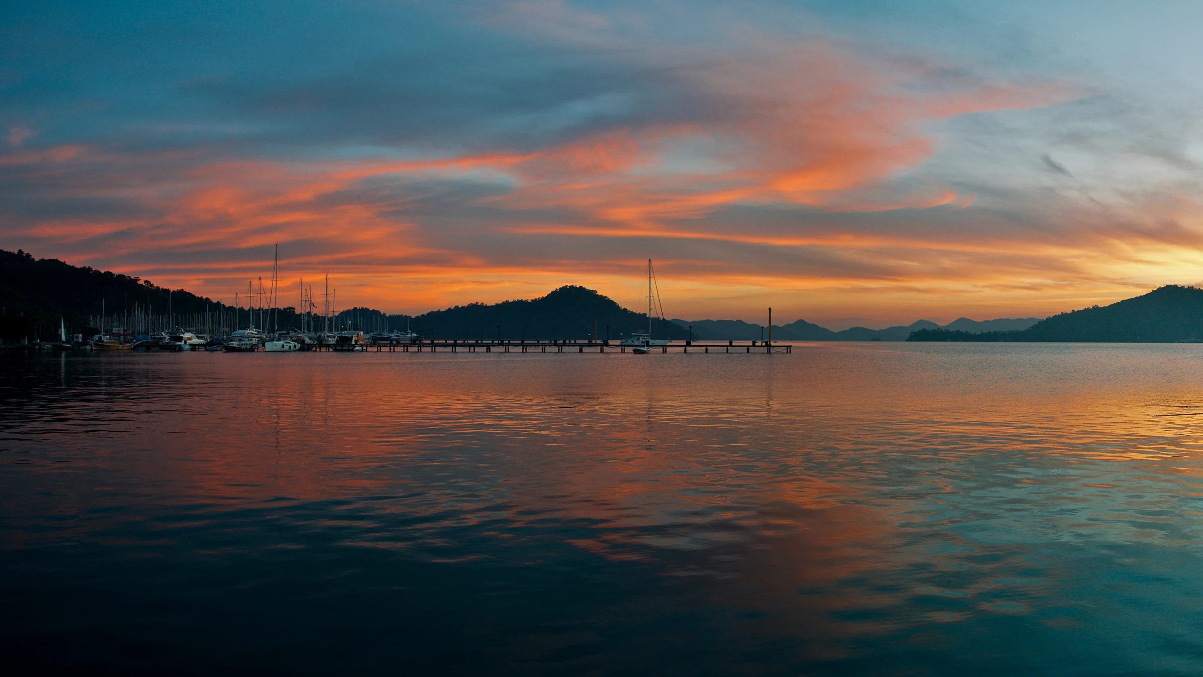 Göcek'te gün batımı manzarası; denizin üzerinde batan güneş ve teknelerin silüetleri. Marina ve koylarda romantik ve huzurlu bir akşam anı.