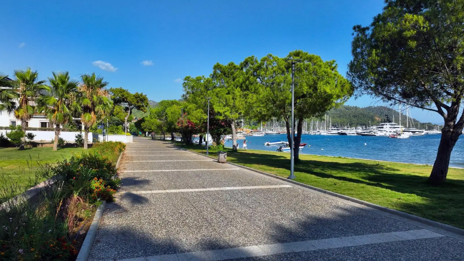 Göcek sahil bandında (kordon) yürüyüş yapan insanlar. Marinadaki tekneler ve restoranlar eşliğinde, özellikle akşamları keyifli bir yürüyüş rotası.