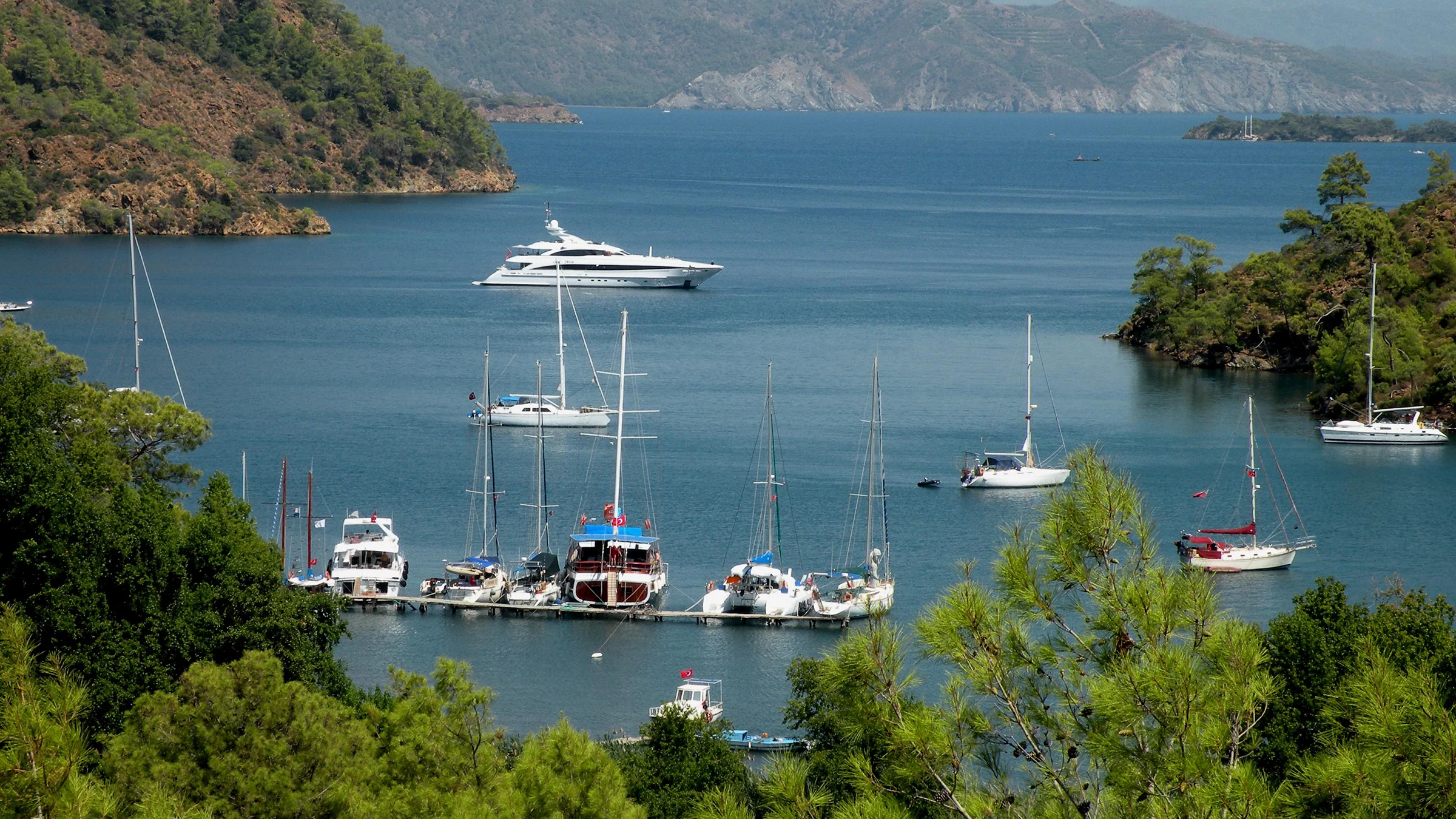 Göcek Boynuzbükü Koyu'nda demirlemiş tekneler ve yemyeşil ağaçlarla çevrili sahil. Göcek'in sakin ve huzurlu mola noktalarından biri.